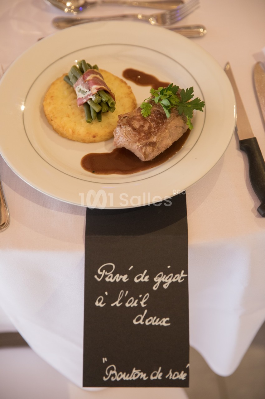 Assiette dressée avec gigot d'agneau, haricots verts enroulés de lard, galette de pommes de terre et sauce.