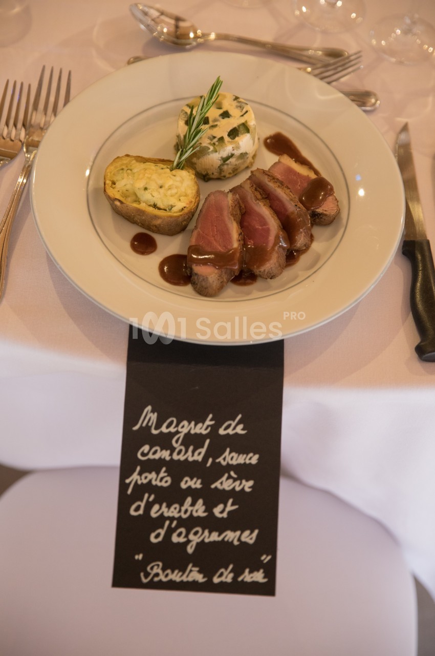 Assiette de magret de canard avec sauce, flan aux herbes et garniture, présentée sur une table dressée.