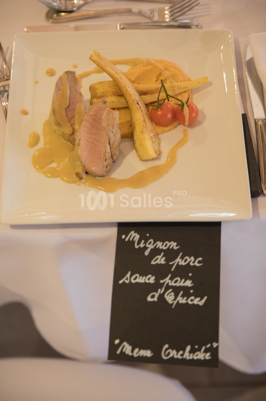 Assiette de mignon de porc avec sauce épicée, purée, panais rôtis et tomates cerises, servie sur une table dressée.