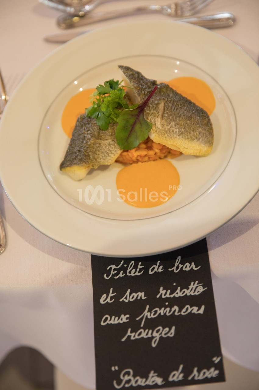 Assiette de filet de bar sur risotto aux poivrons rouges, décorée de verdure et sauce orangée.
