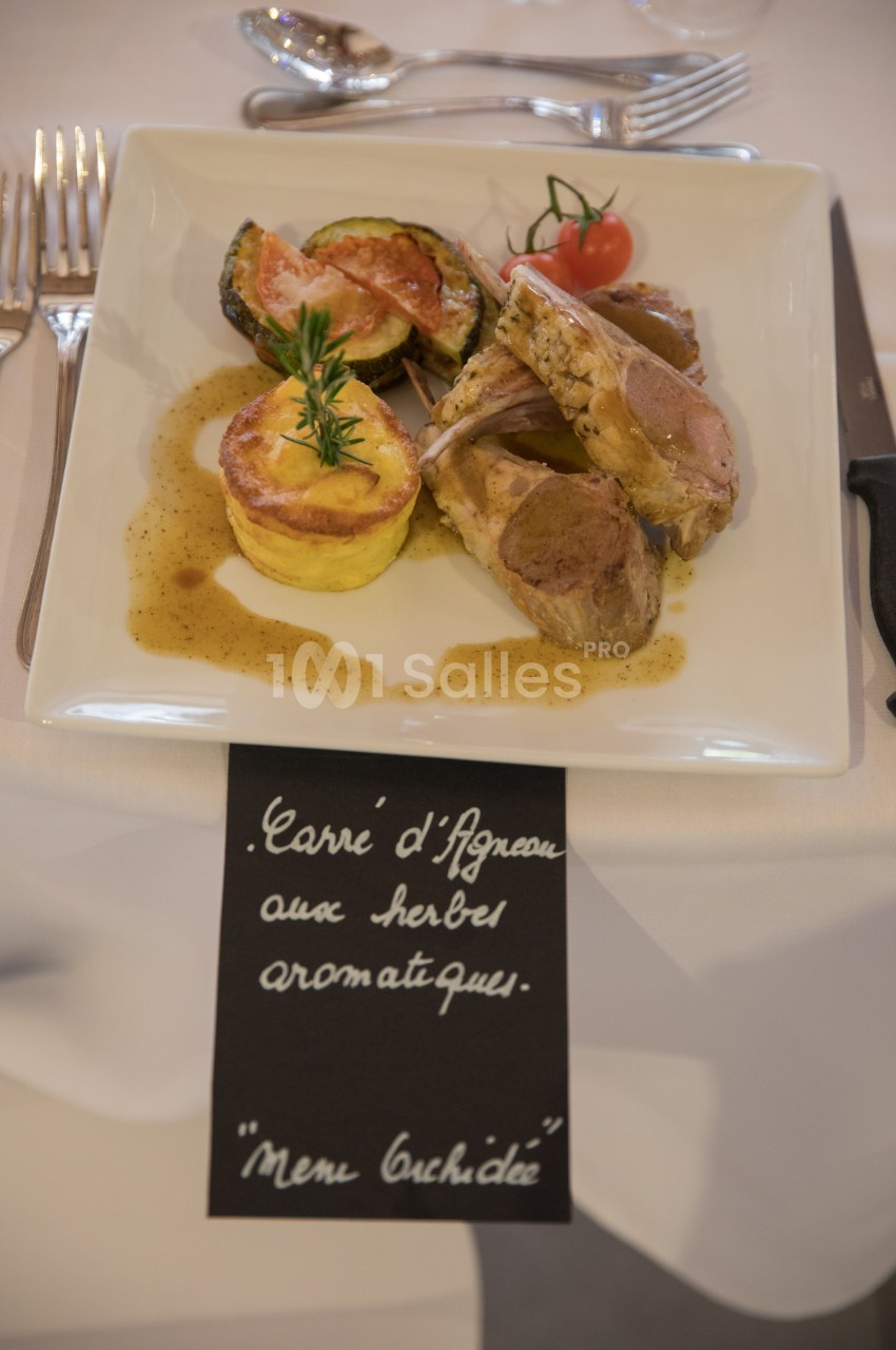 Assiette de carré d'agneau avec gratin, légumes grillés et sauce, servie sur une table dressée.
