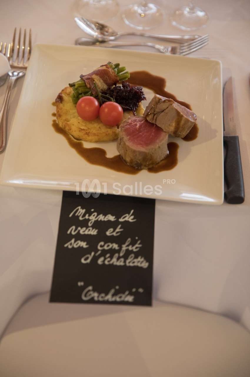 Assiette de mignon de veau avec légumes, tomates cerises, purée et sauce, servie sur une table dressée.
