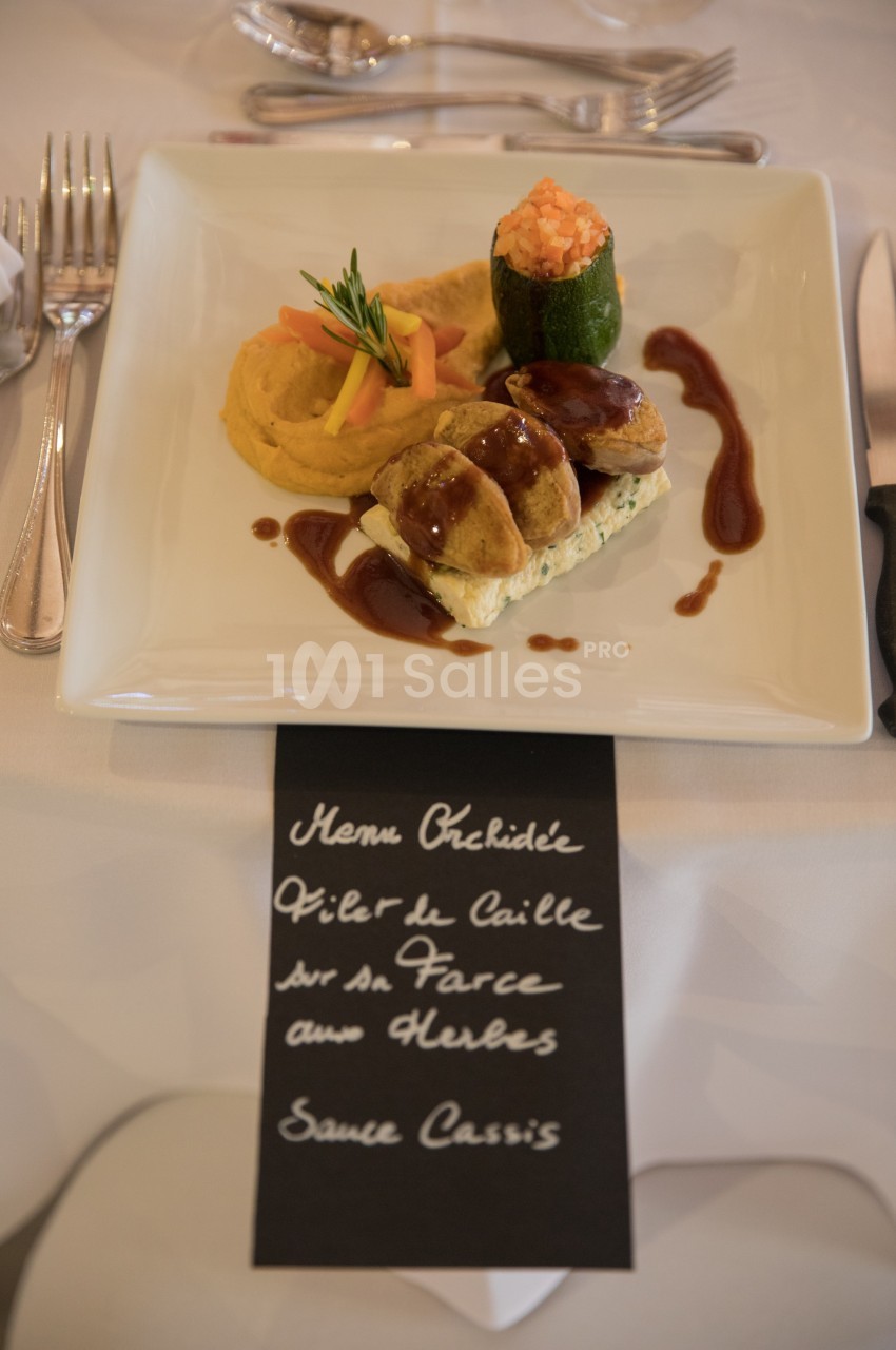 Assiette gastronomique avec filet de caille, purée, courgette farcie et sauce cassis, présentée sur une table dressée.