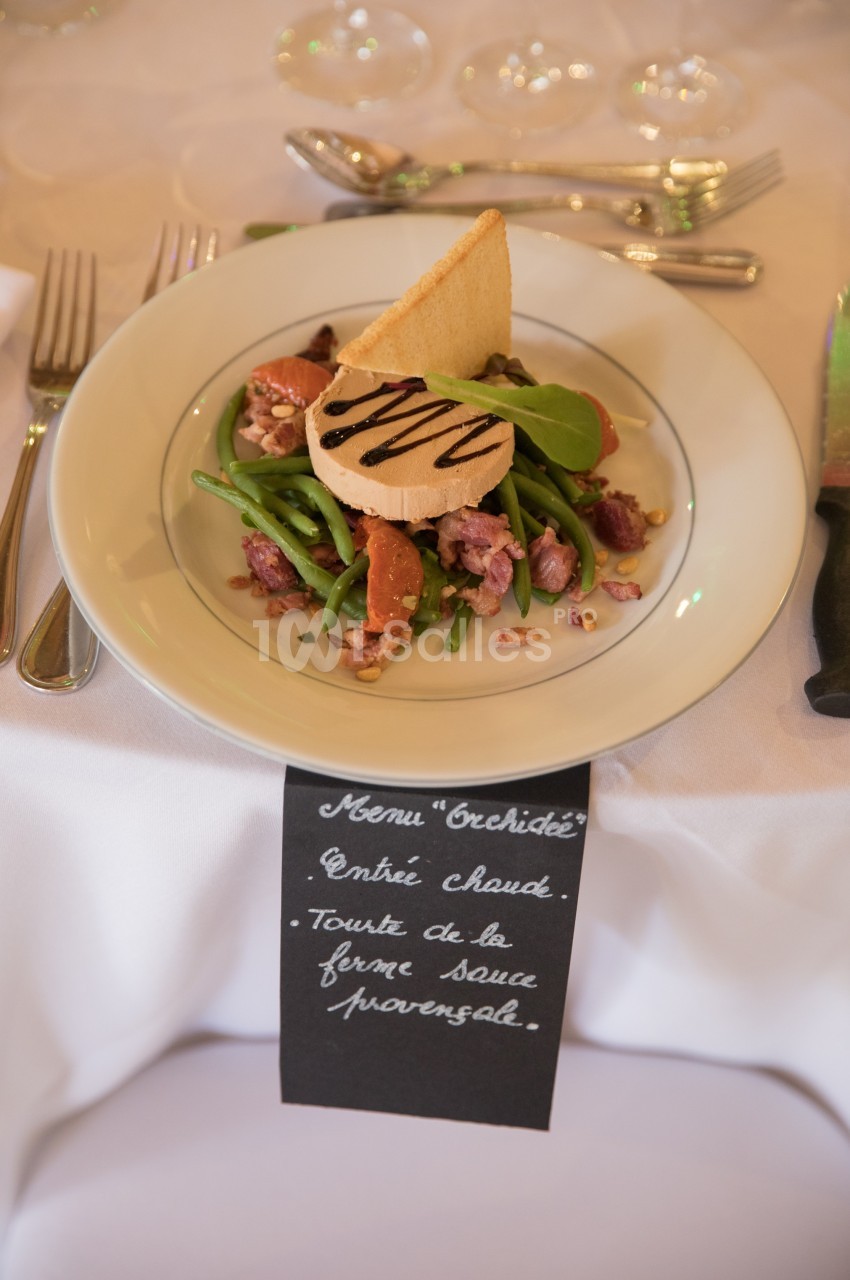 Assiette de salade composée avec haricots verts, magret de canard, noix, toast et sauce, présentée sur une table dressée.