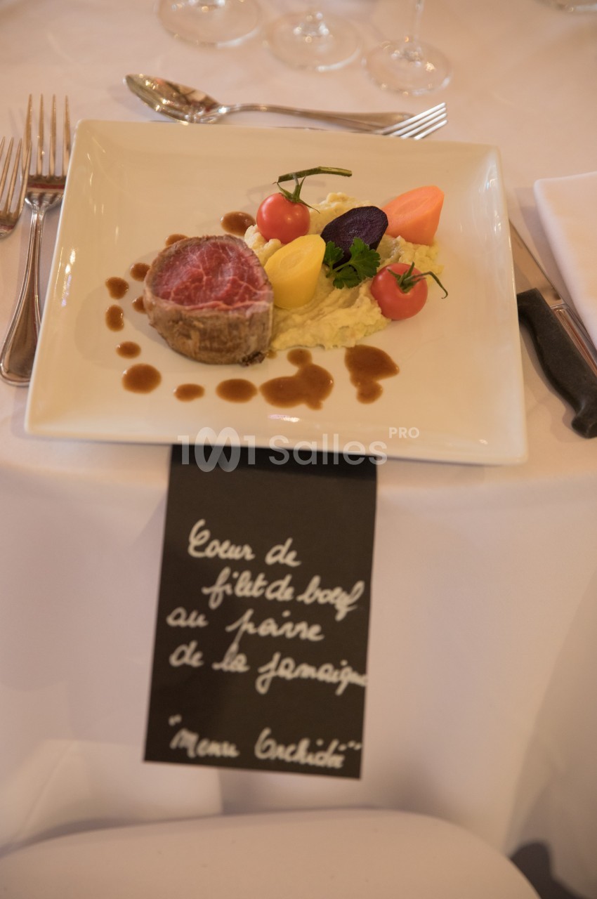 Assiette gastronomique avec filet de bœuf, légumes colorés, purée et sauce, présentée sur une table dressée.