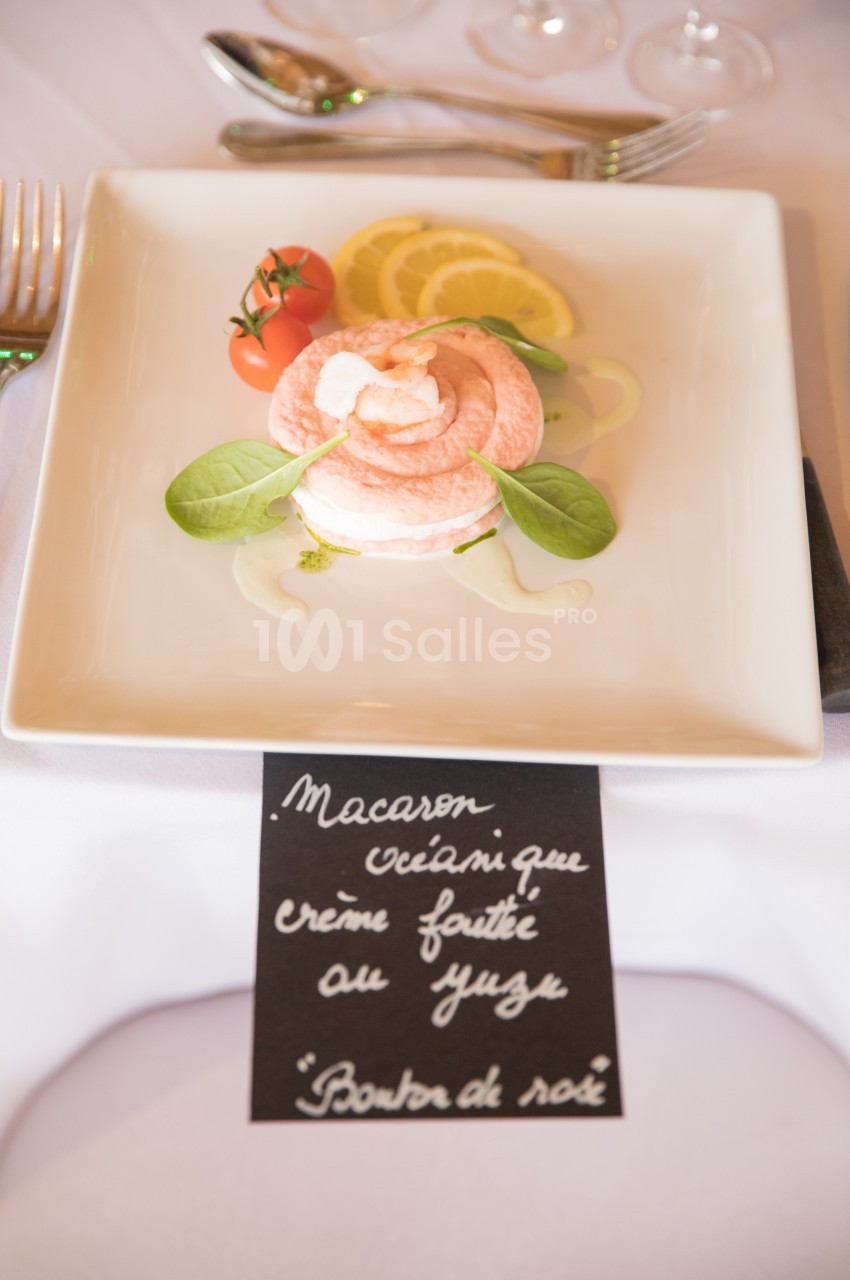 Assiette contenant un macaron rose garni de crème, accompagné de tomates cerises, citron et feuilles de salade.