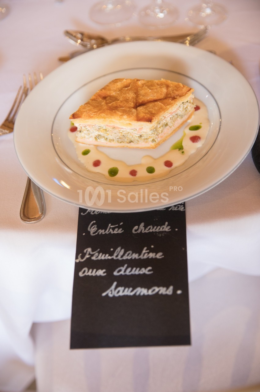 Part de feuilleté au saumon servie sur une assiette blanche avec décoration de sauce colorée.