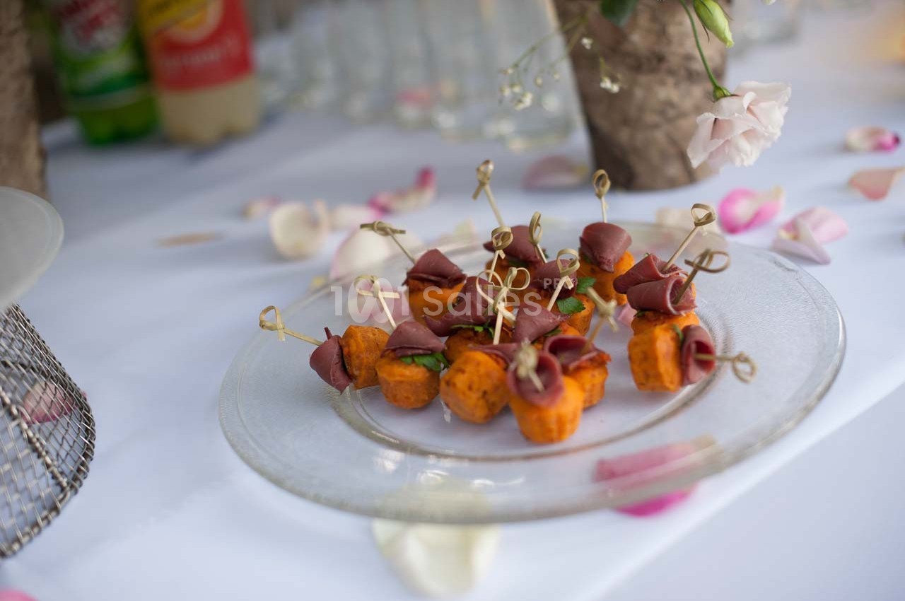 Assiette de bouchées apéritives composées de patates douces et de viande roulée, présentée sur une table décorée.