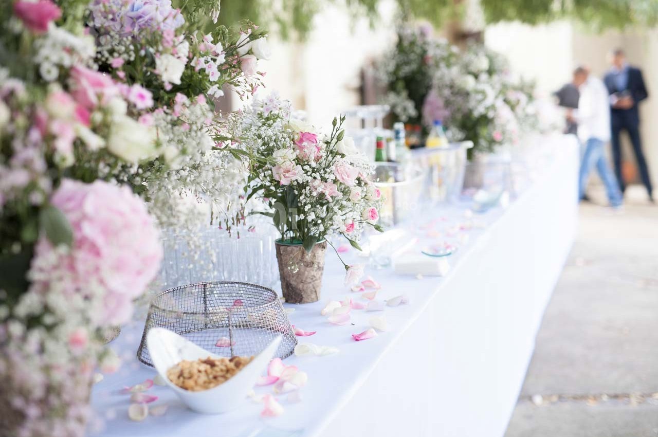 Table décorée avec des fleurs, pétales roses et blancs, contenant des boissons et des amuse-bouches en extérieur.