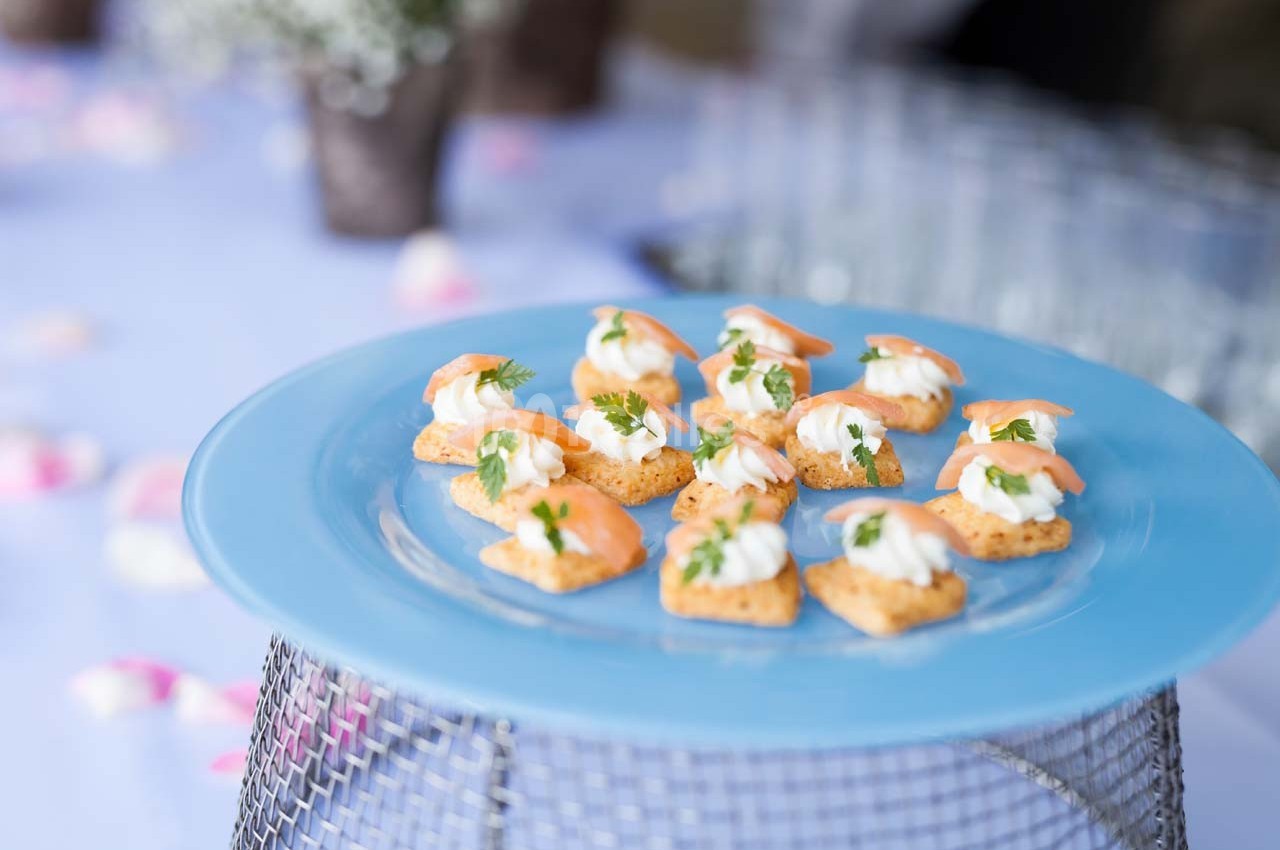 Assortiment de canapés au saumon et crème sur un plateau bleu, présenté sur une table décorée.