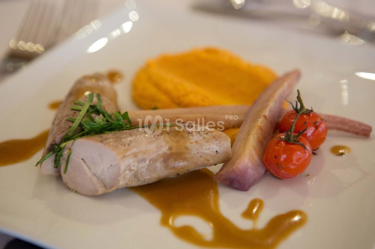 Assiette gastronomique avec filet de viande, purée orange, tomates cerises et sauce, présentée sur une table élégante.