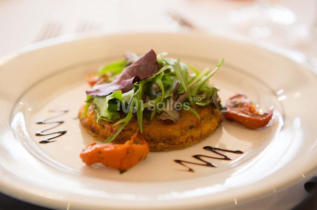 Plat végétarien composé d'une galette de légumes, de feuilles de salade et de tomates rôties, décoré de sauce balsamique.