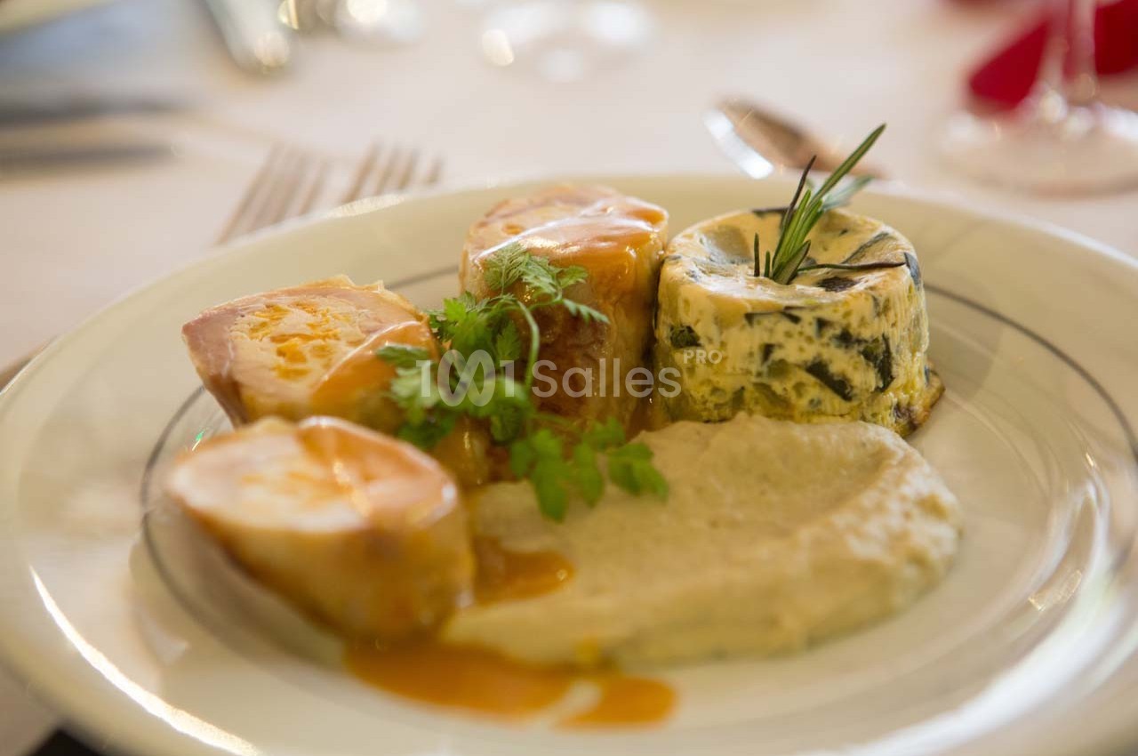 Assiette contenant des morceaux de viande, une purée, un flan aux légumes et une garniture d'herbes fraîches.