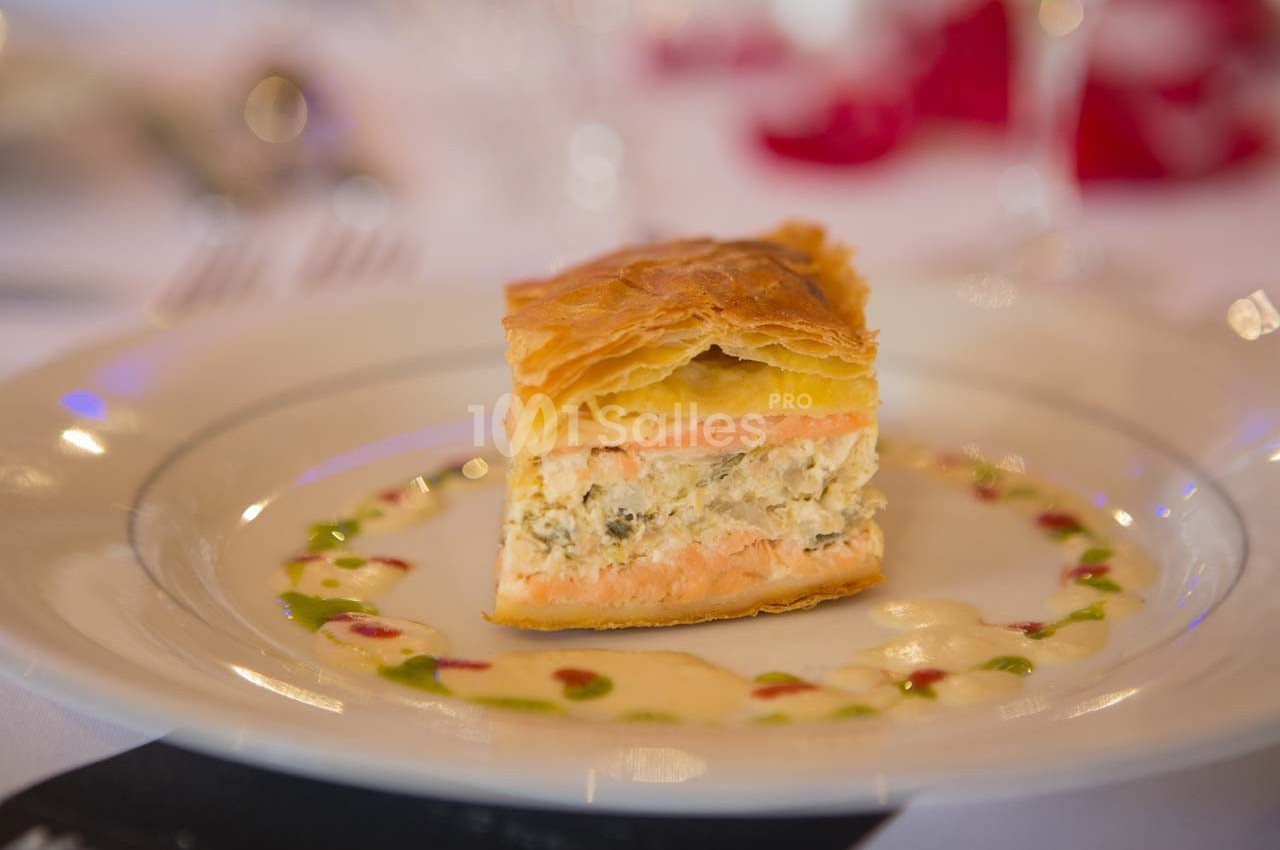 Part de feuilleté au saumon et farce crémeuse, servie sur une assiette avec une sauce décorative colorée.