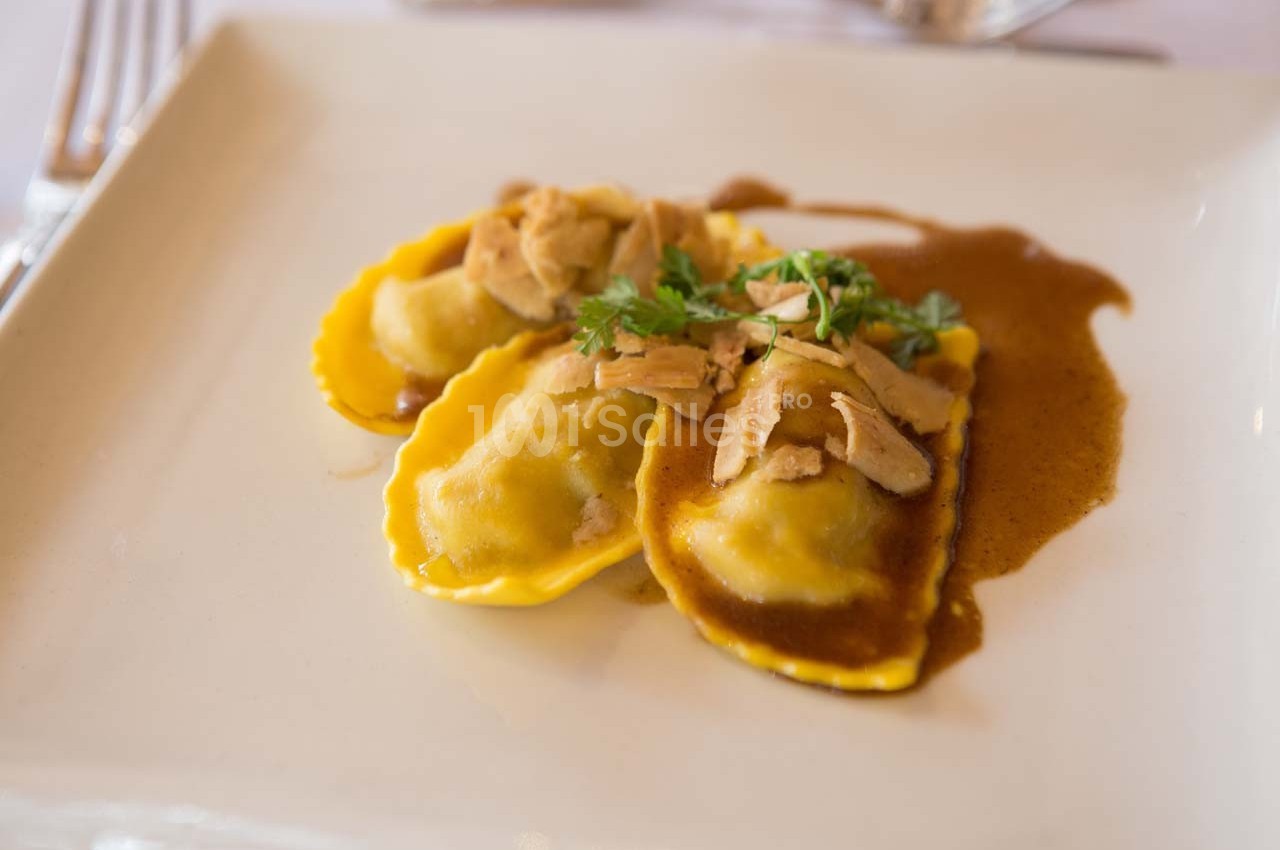 Assiette de raviolis garnis, nappés de sauce brune, garnis de morceaux de viande et de persil frais.