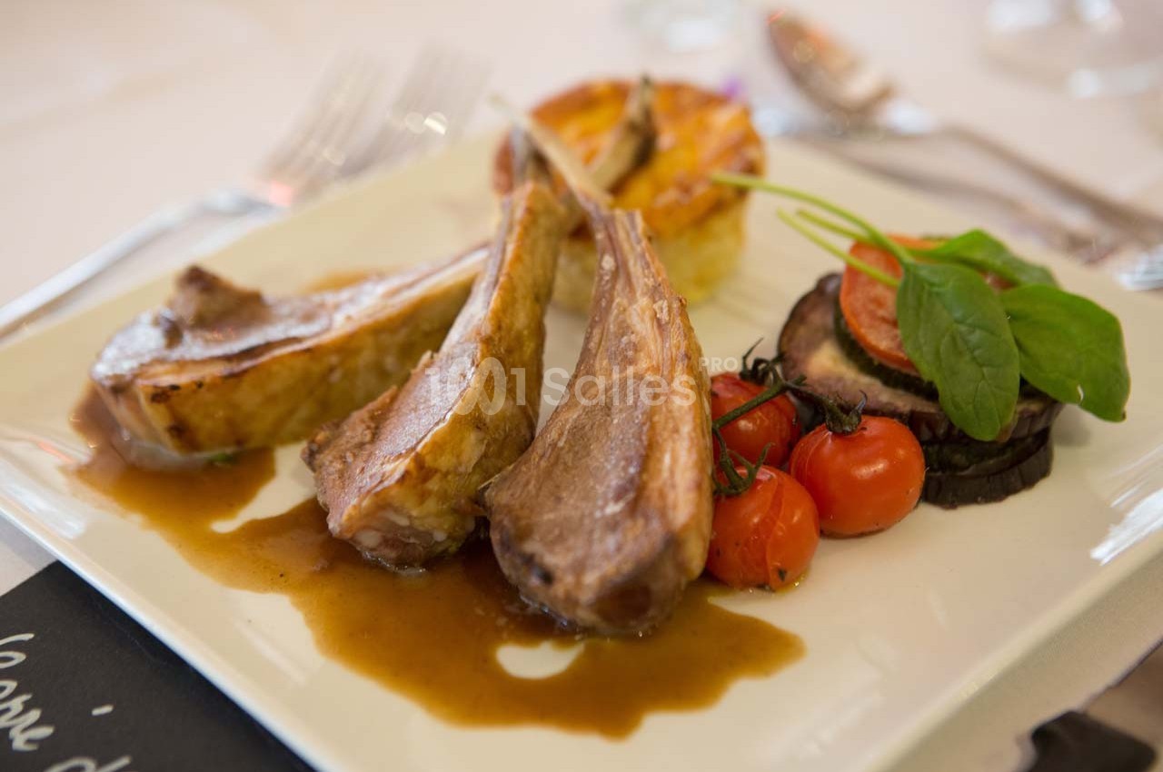 Assiette de côtelettes d'agneau avec sauce, légumes grillés, tomates cerises et accompagnement de pommes de terre.