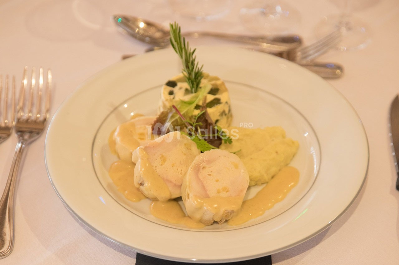 Assiette de médaillons de volaille nappés de sauce, accompagnés de purée et d'un flan aux herbes.