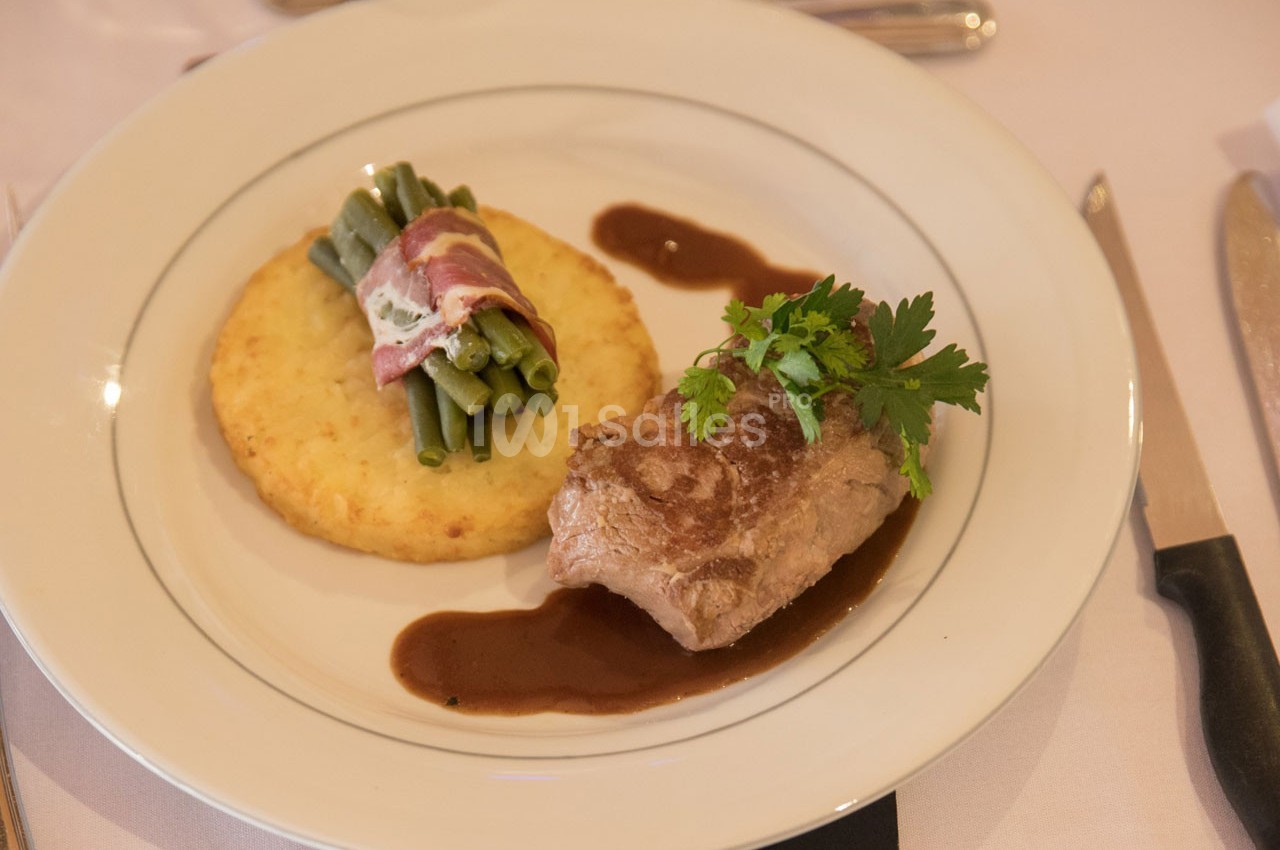 Assiette composée d'un médaillon de viande, d'une galette de pommes de terre, de haricots verts enroulés de lard et d'une…