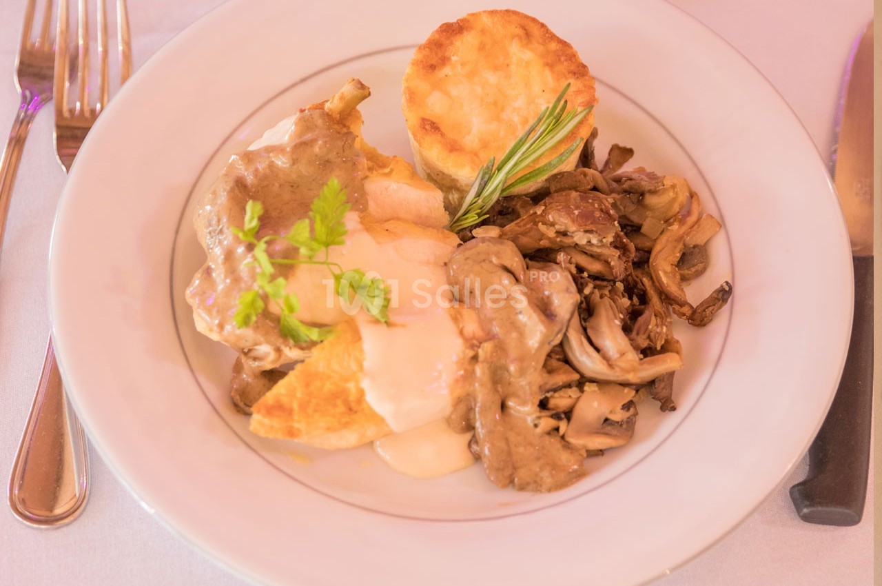 Assiette contenant un plat de volaille avec sauce, champignons, gratin et un petit flan, servie sur une table dressée.