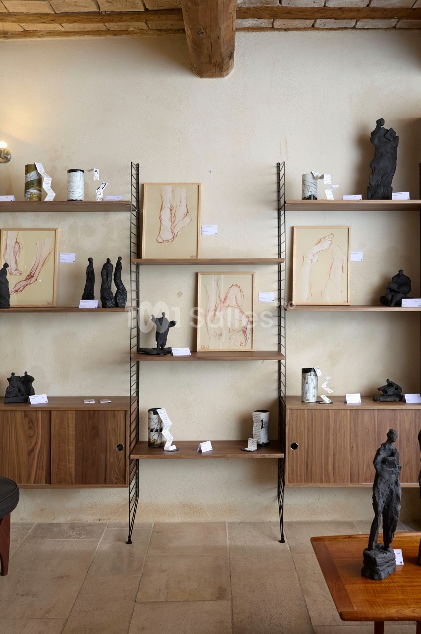 Étagères en bois et métal exposant des sculptures et dessins artistiques dans une pièce au mur beige et au plafond en…