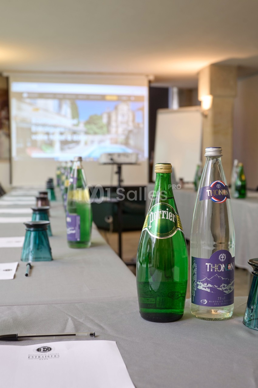 Bouteilles d'eau minérale posées sur une table de réunion avec écran de présentation flou en arrière-plan.
