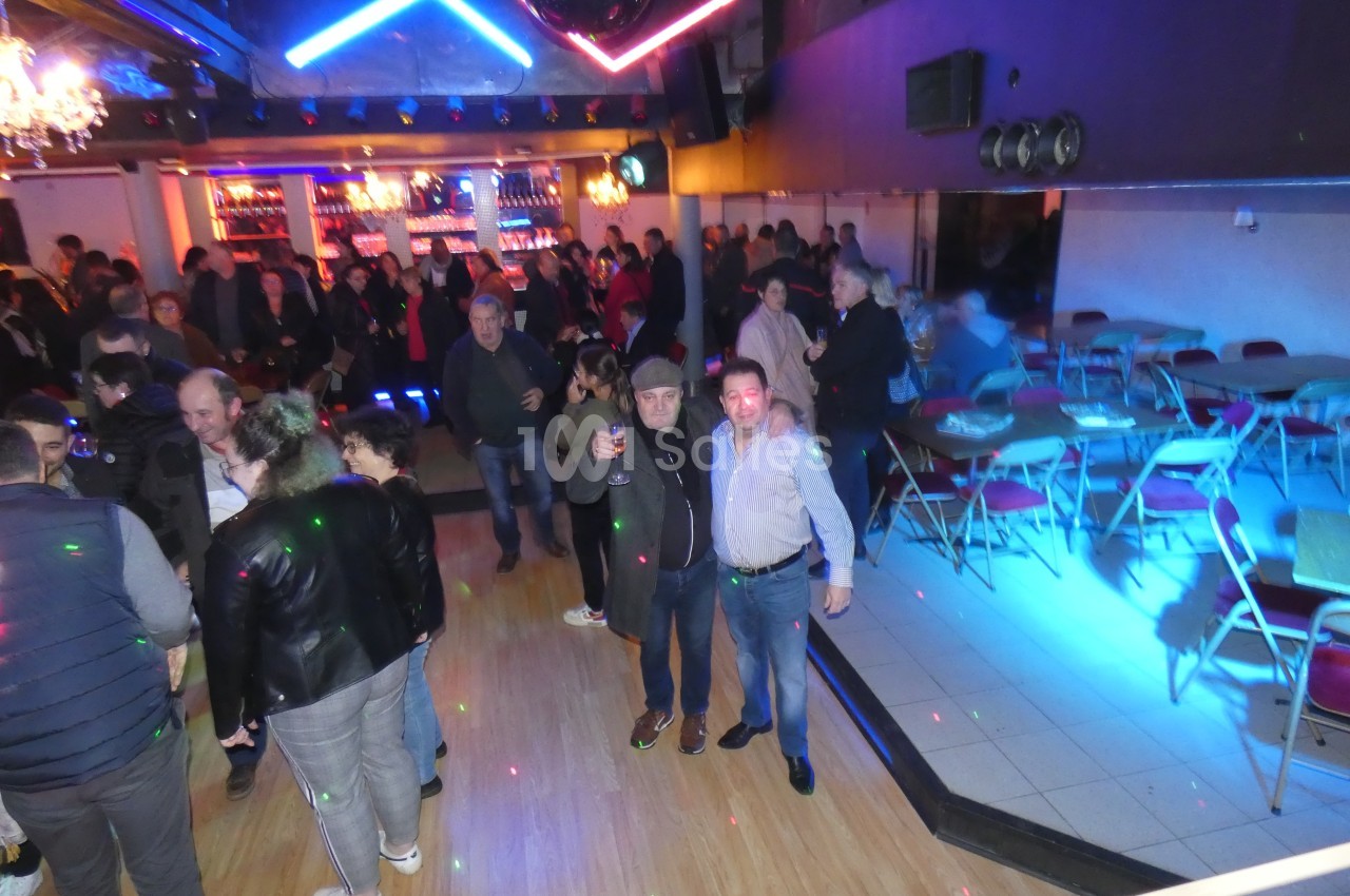 Personnes rassemblées dans une salle de fête éclairée, avec piste de danse et tables sur le côté.