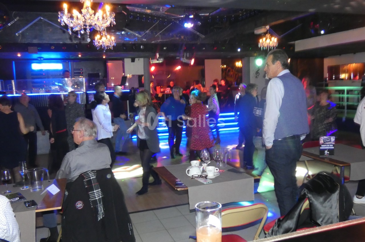 Des personnes dansent et discutent dans une salle animée avec éclairages colorés et ambiance festive.