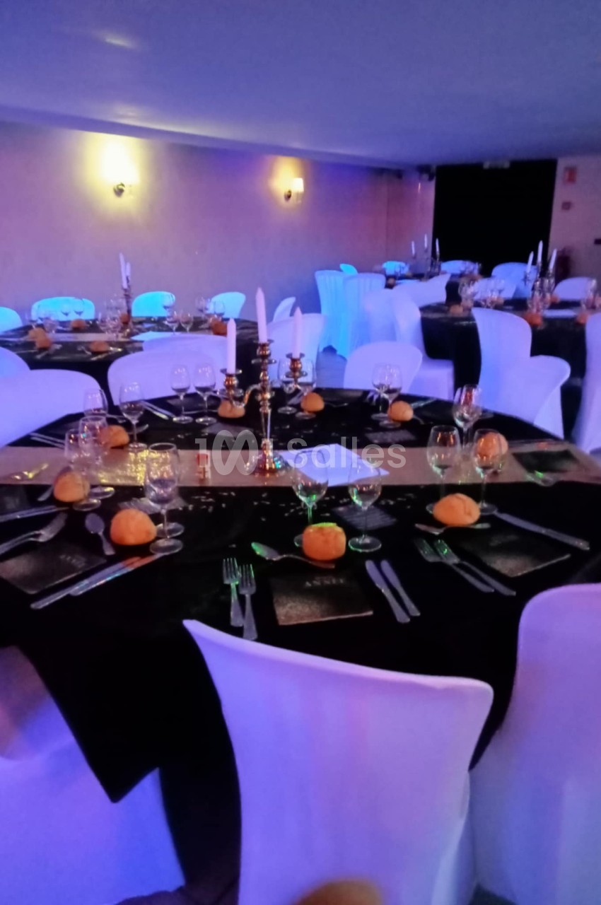 Salle de réception décorée avec des tables rondes, nappes noires, bougeoirs dorés et petites citrouilles en centre de table.