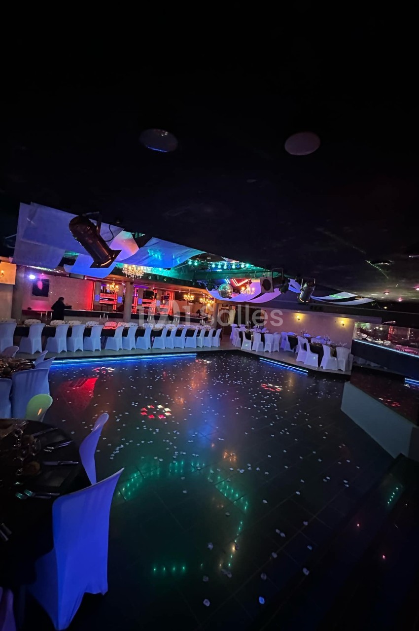 Salle de réception avec piste de danse illuminée, tables dressées et éclairage coloré dans une ambiance festive.
