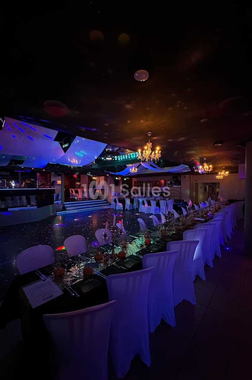 Salle de réception décorée avec des tables dressées, éclairage tamisé et ambiance festive.