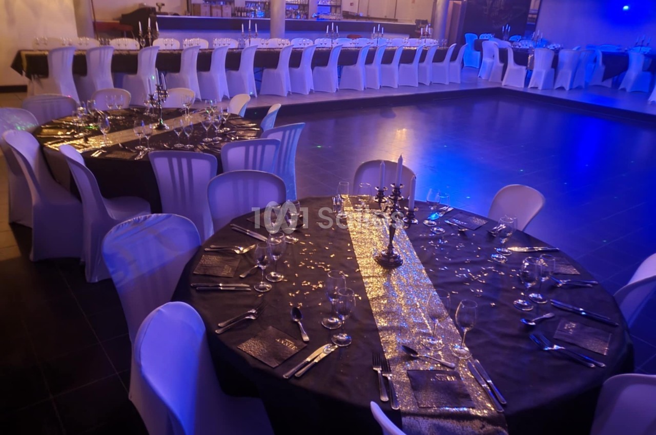 Salle de réception décorée avec des tables rondes et rectangulaires, nappes noires, couverts élégants et éclairage tamisé.
