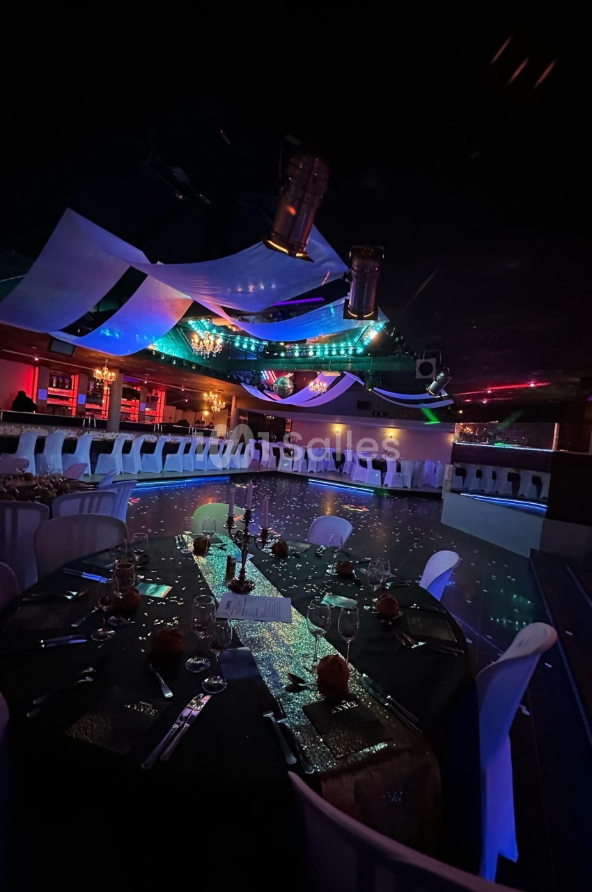 Salle de réception décorée avec des tables dressées, piste de danse illuminée et éclairages colorés au plafond.