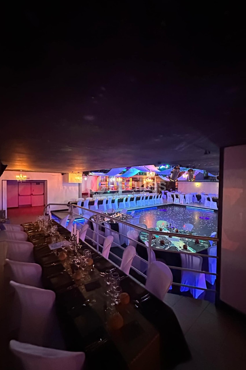 Salle de réception élégante avec tables dressées, éclairage tamisé et vue sur une piscine illuminée.