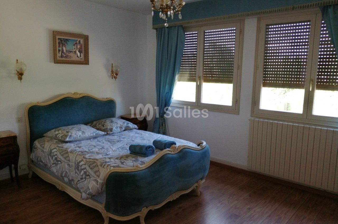 Chambre lumineuse avec lit double à tête de lit bleue, rideaux assortis, parquet et décoration classique.