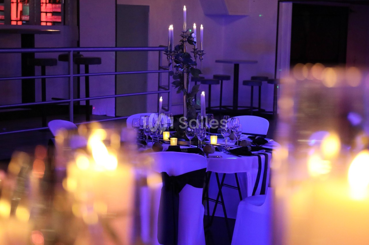 Table élégamment dressée avec chandeliers et bougies allumées dans une ambiance tamisée et violette.