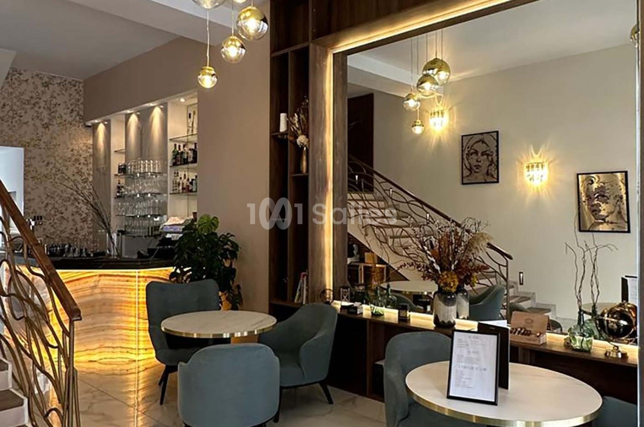 Intérieur d'un café moderne avec tables rondes, chaises rembourrées, grand miroir et comptoir lumineux.