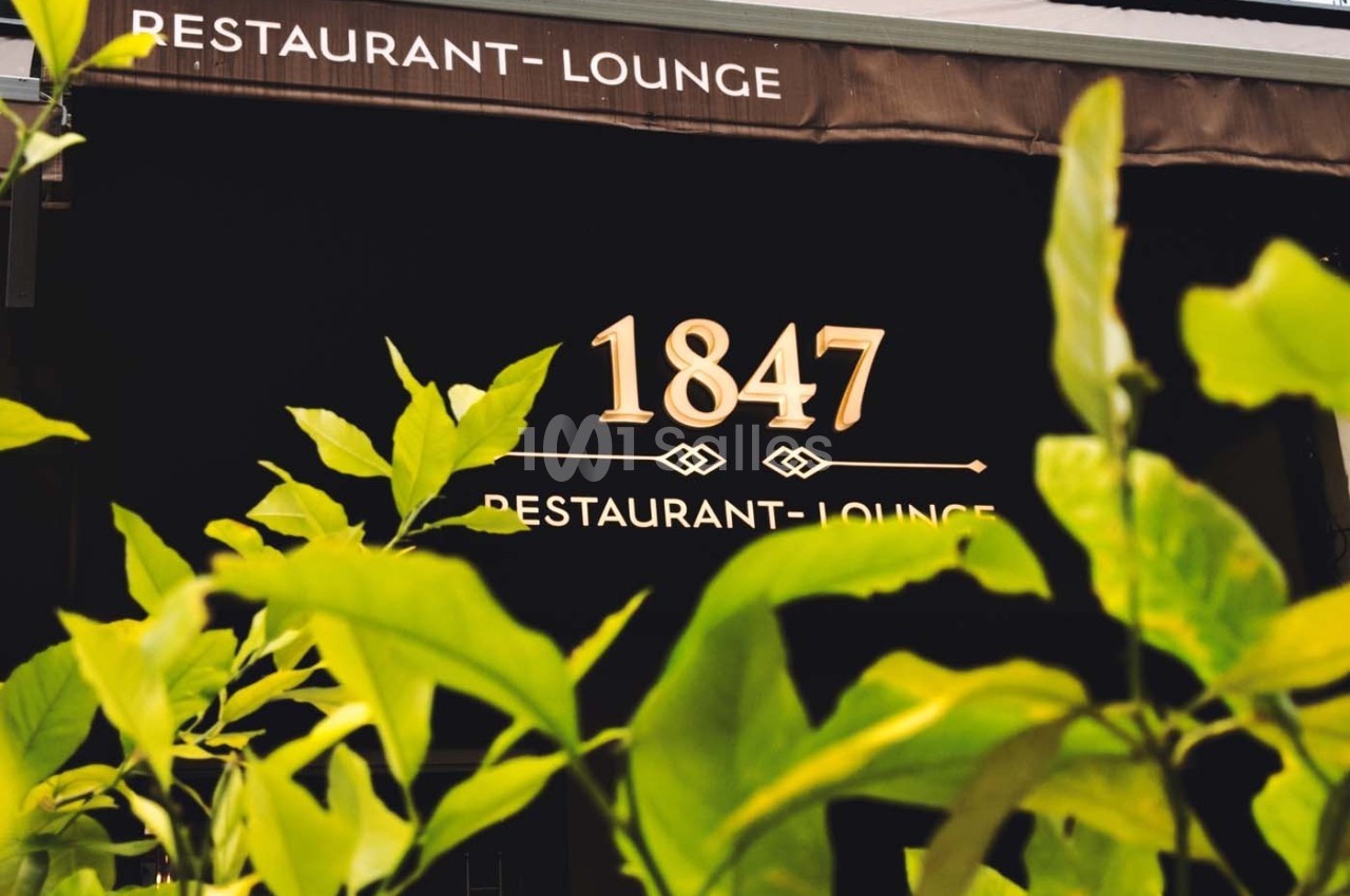 Façade d'un restaurant avec l'inscription ’1847 Restaurant-Lounge’, partiellement cachée par des feuilles vertes au premier…