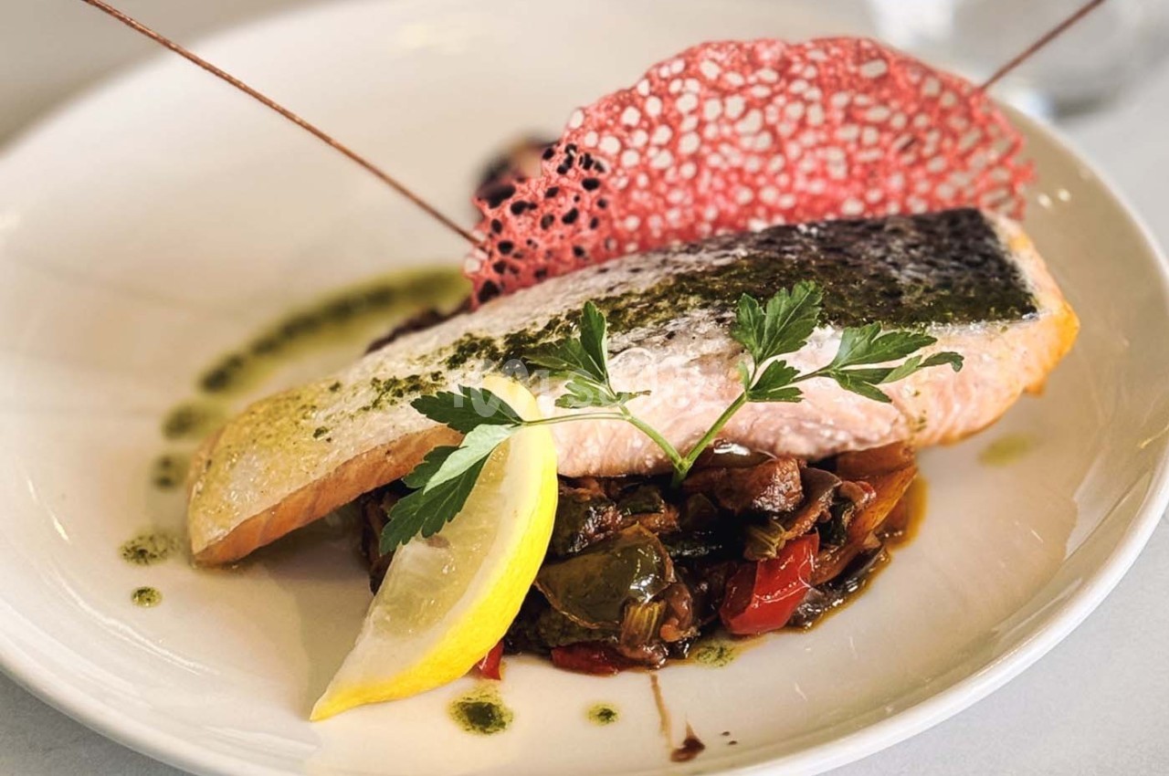 Filet de saumon grillé sur lit de légumes sautés, décoré de persil, citron et tuile rouge croustillante.