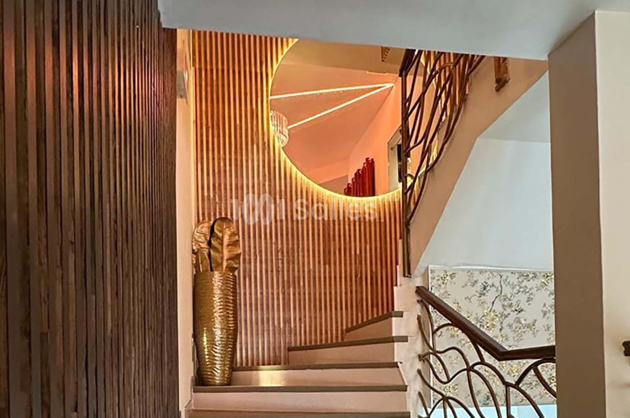Escalier intérieur avec mur en bois, miroir rond rétroéclairé et vase doré décoratif au pied des marches.