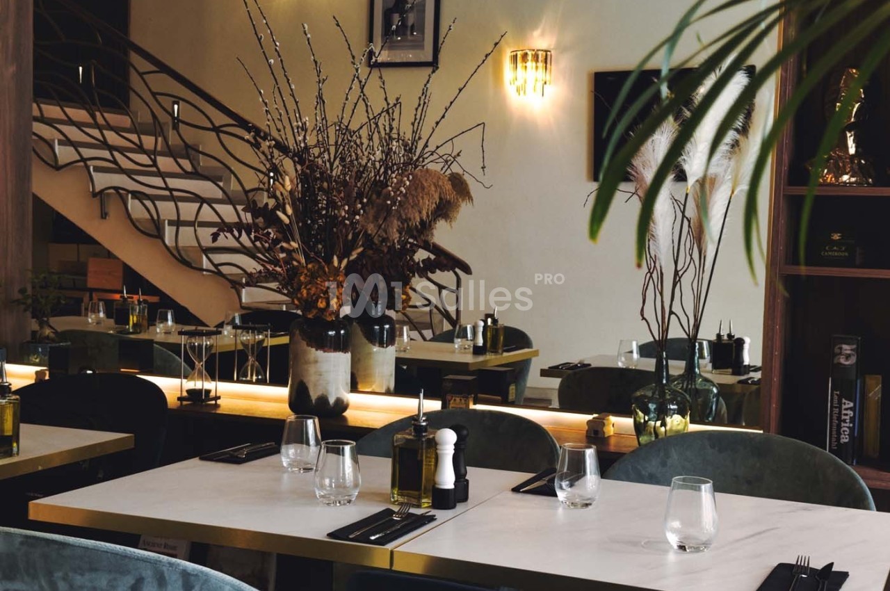 Salle de restaurant élégante avec tables dressées, décorée de plantes et d'un grand bouquet de branches sèches.