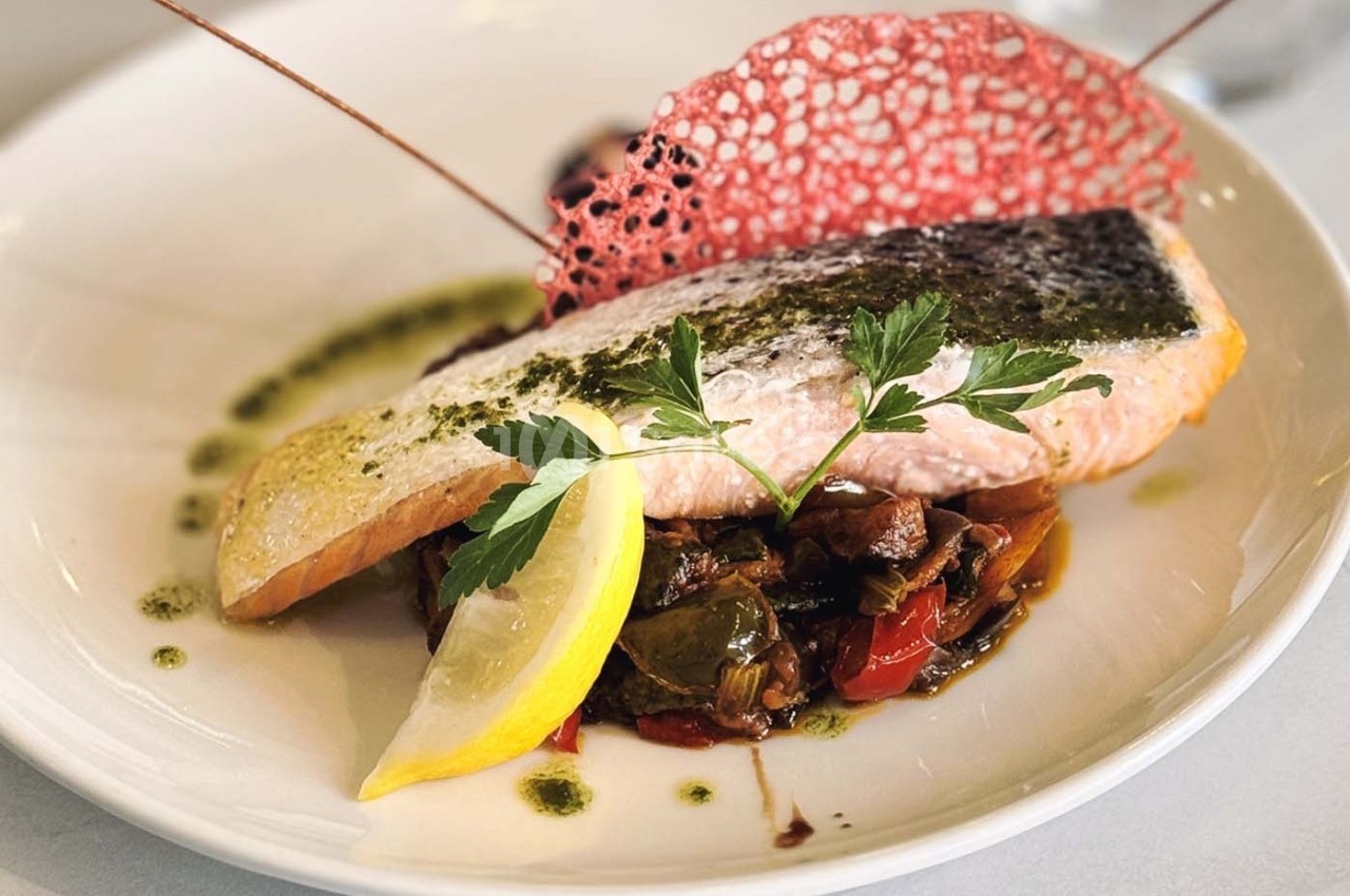 Filet de saumon grillé sur légumes sautés, décoré d'une tuile rouge, d'herbes fraîches et d'un quartier de citron.