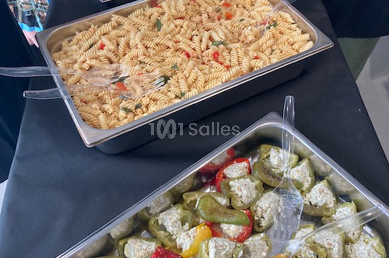 Plateaux de buffet contenant des pâtes torsadées aux légumes et des poivrons farcis au fromage sur une nappe noire.