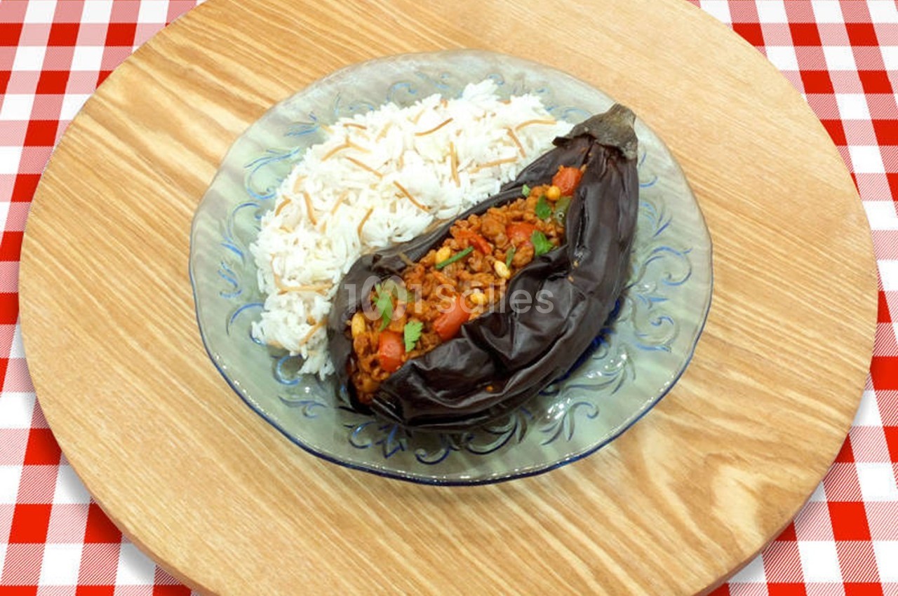 Aubergine farcie garnie de légumes et servie avec du riz blanc sur une assiette en verre, posée sur une table en bois.