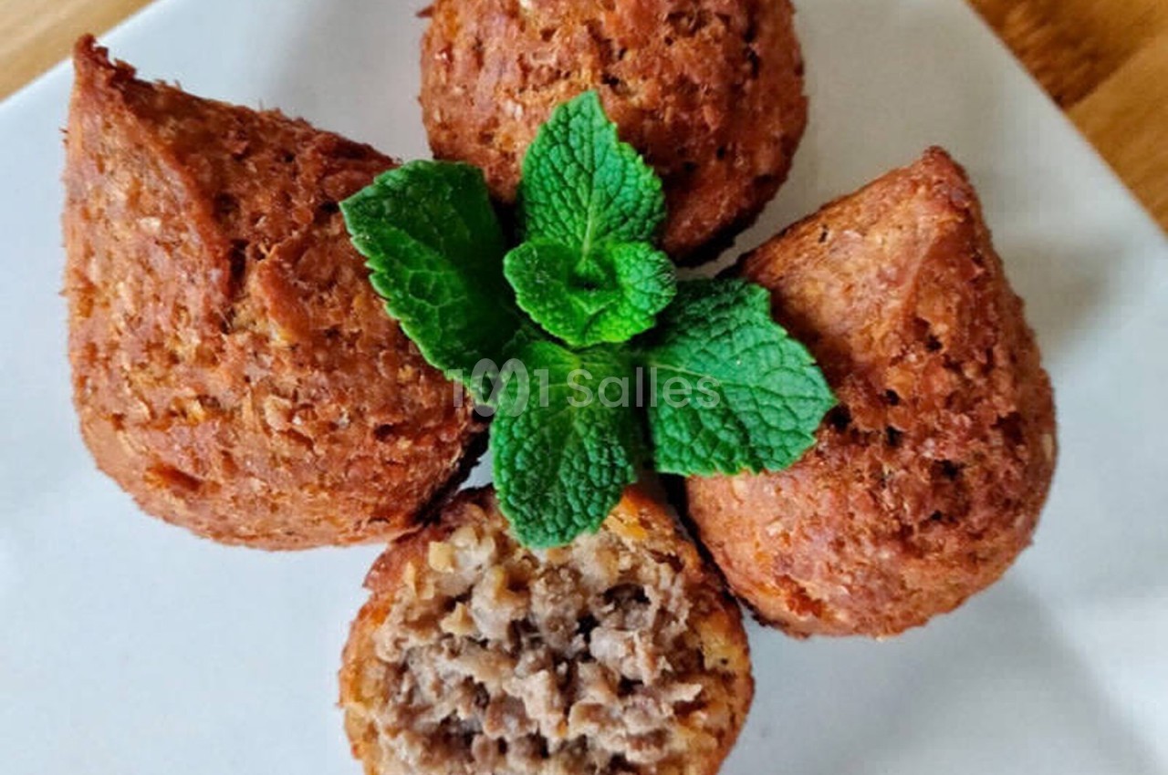 Quatre kibbeh dorés disposés en fleur sur une assiette blanche, garnis de feuilles de menthe fraîche.