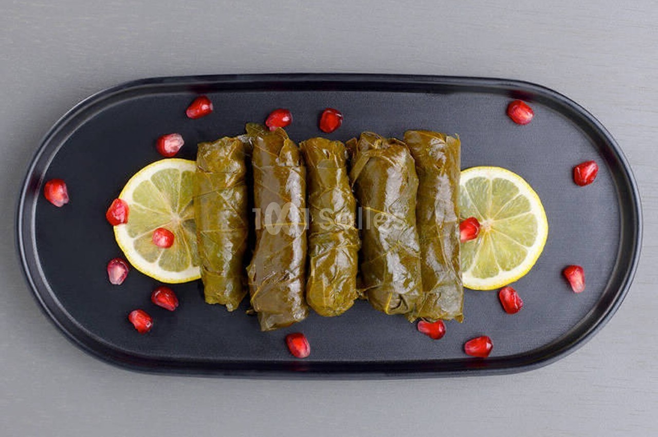 Feuilles de vigne farcies alignées sur une assiette noire, décorées de rondelles de citron et grains de grenade.