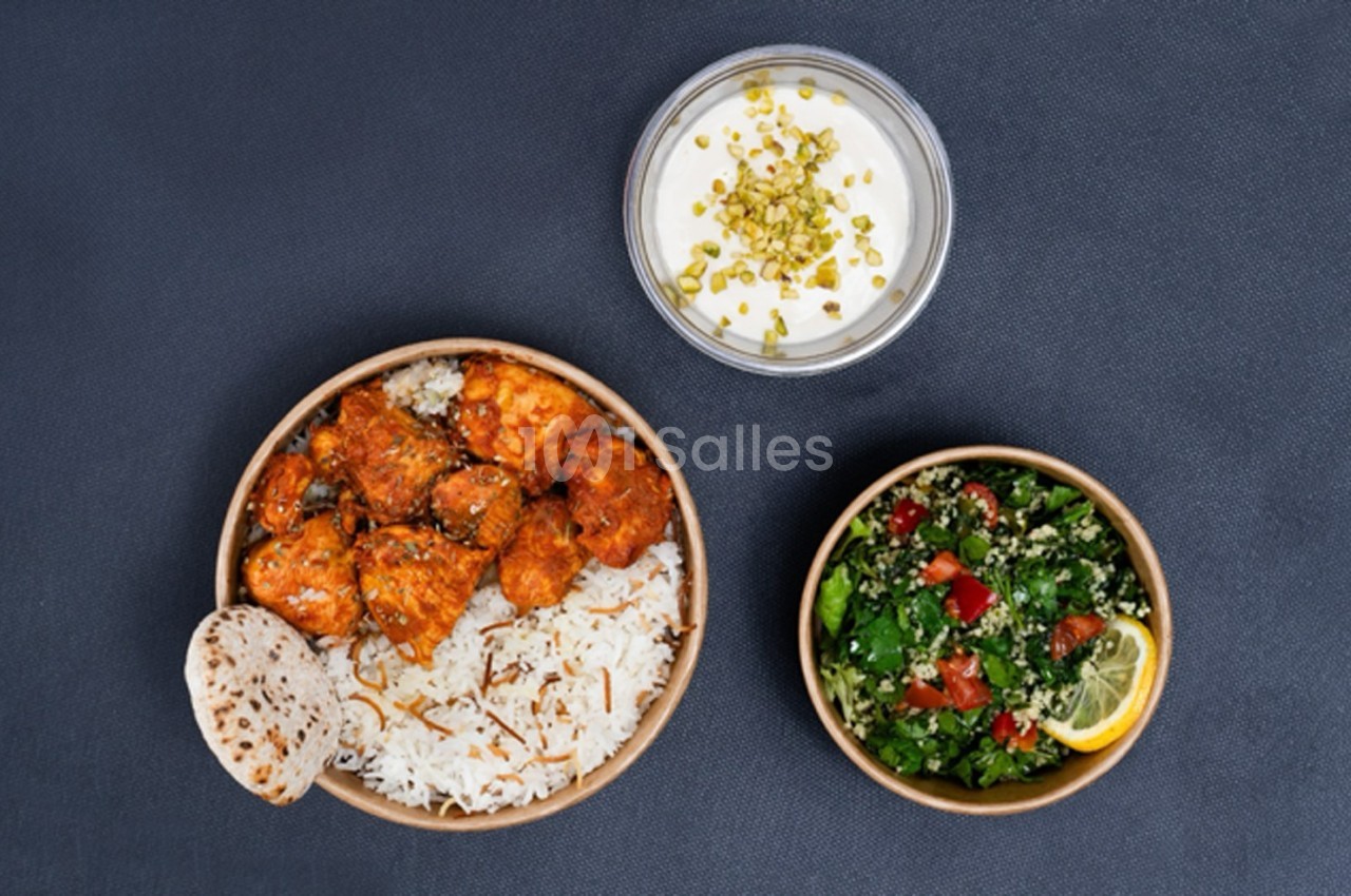 Assiette de poulet épicé avec riz, pain plat, accompagnée d'une salade fraîche et d'une sauce au yaourt garnie de pistaches.