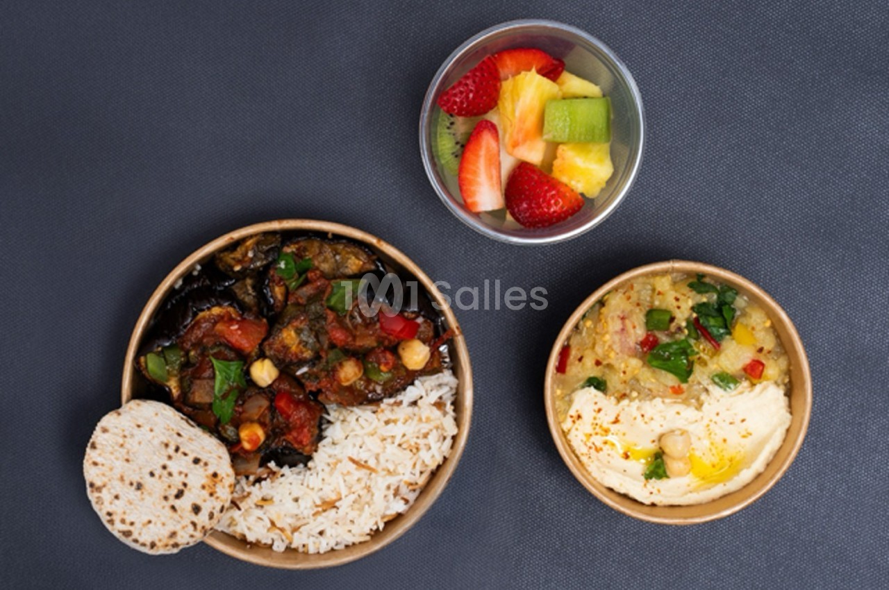Assiette avec riz, légumes sautés, pain plat, bol de houmous et salade, accompagnée d'une coupe de fruits frais.
