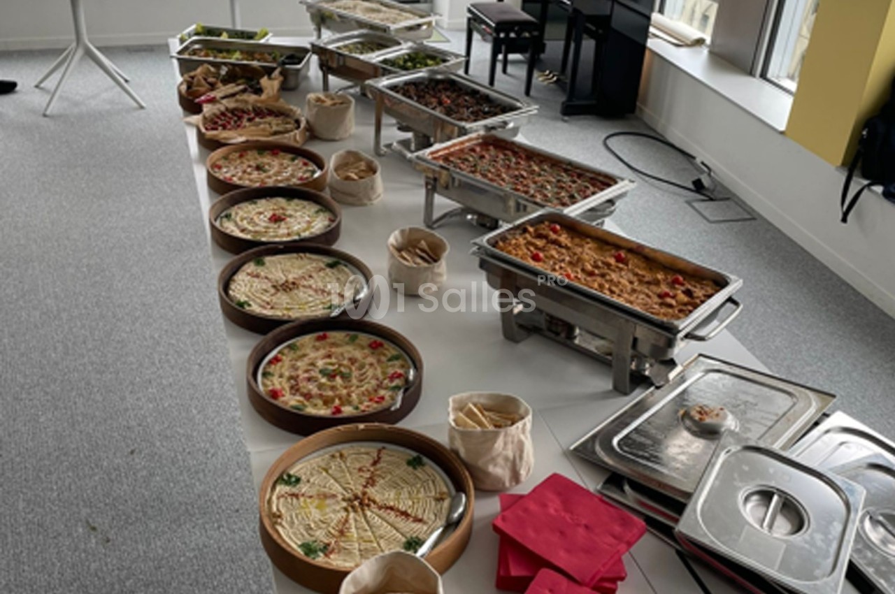 Buffet avec plats variés, incluant quiches, gratins et salades, disposés sur une table dans une salle lumineuse.