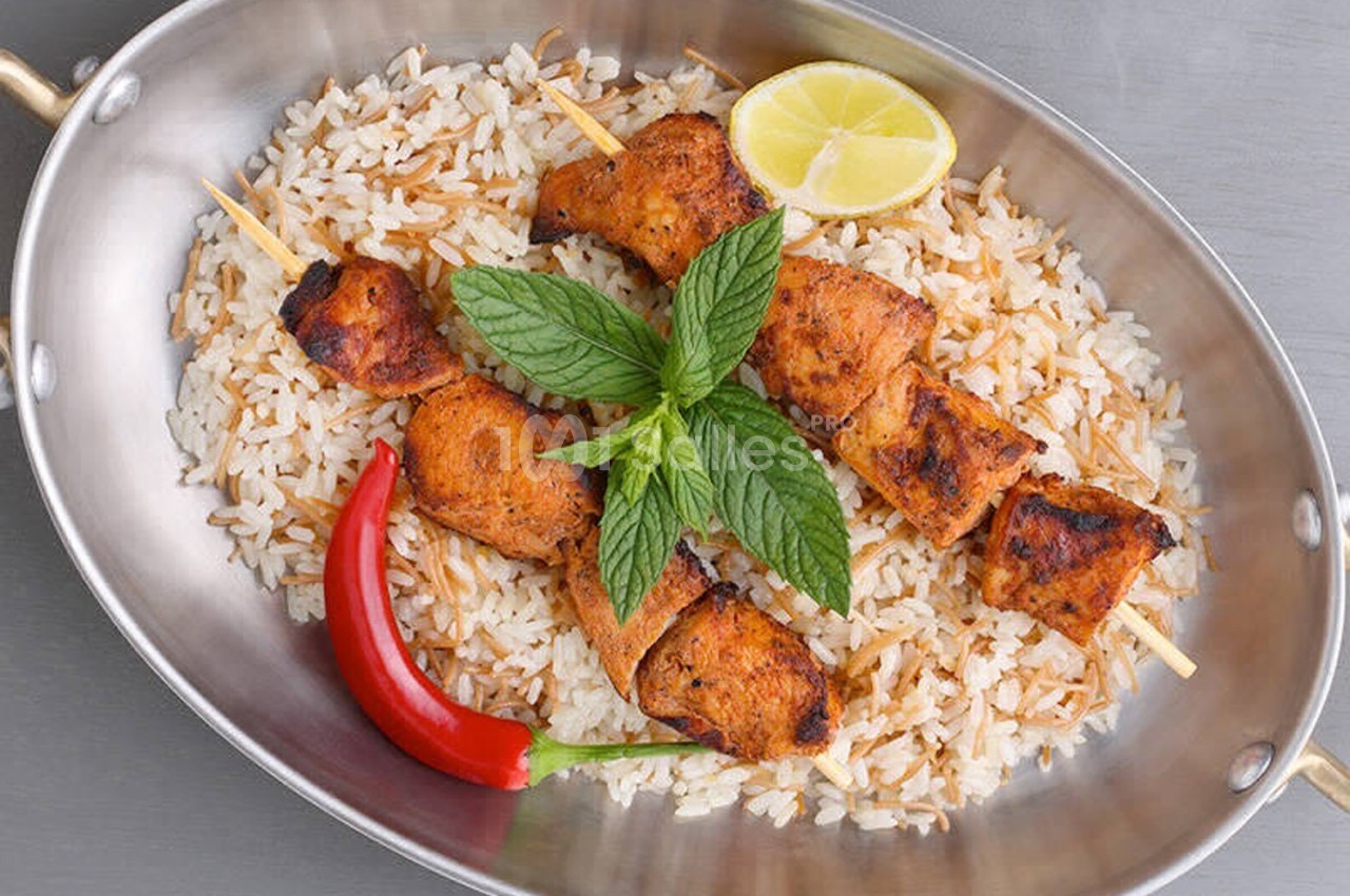 Brochettes de poulet grillé servies sur un lit de riz avec un piment rouge, une rondelle de citron et des feuilles de menthe.