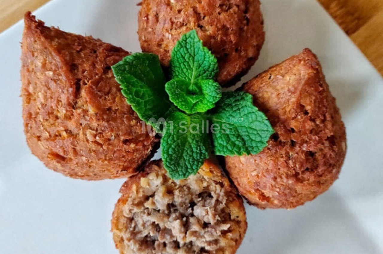 Quatre kibbeh dorés disposés en étoile sur une assiette blanche, garnis de feuilles de menthe fraîche.
